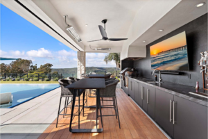 luxury outdoor kitchen with bar seating, ceiling fan, pool view, and modern patio dining area