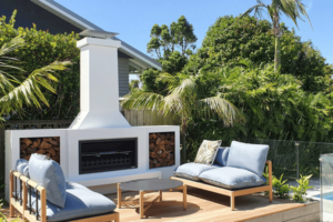 modern outdoor patio with fireplace, wooden seating, cushions, and tropical landscaping