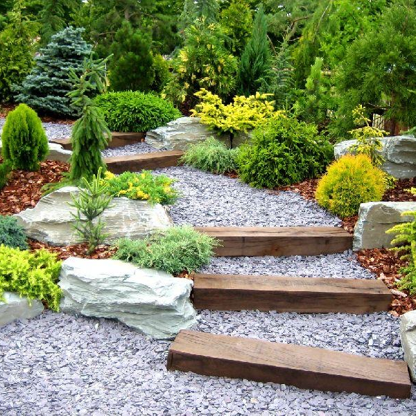 Low-maintenance landscaped yard with gravel pathway, wooden steps, natural stone edging, and native evergreen plants