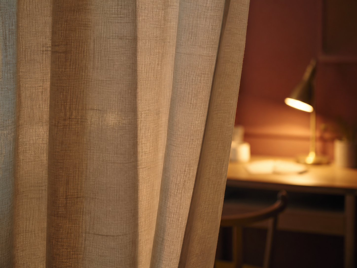 Linen curtain half-drawn across a small desk nook, closing the workspace off from the room