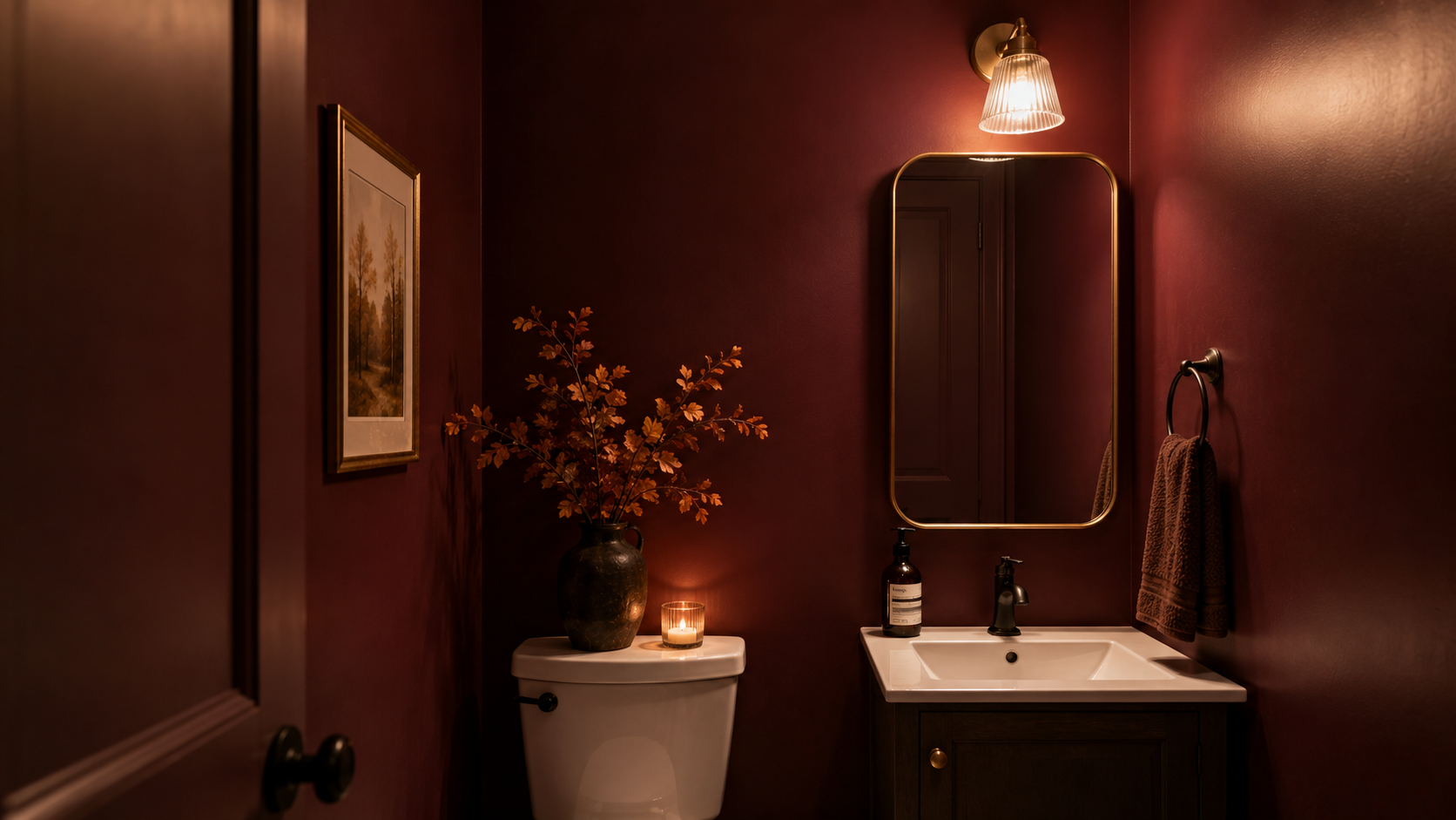 Small powder room fully painted in deep oxblood with brass mirror and cream pedestal sink